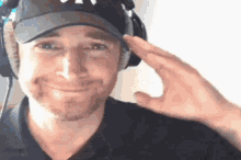 a man wearing a hat and headphones salutes with his hand on his forehead .