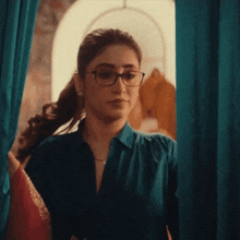 a woman wearing glasses and a blue shirt is looking out a window