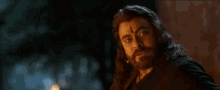 a man with long hair and a beard has a red dot on his forehead .