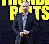 a man in a suit is standing in front of a sign that says thunderbolts