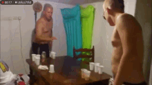 two shirtless men are standing in front of a table with cups and an inflatable raft behind them ..