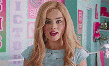 a woman with blonde hair and a blue shirt is standing in front of a wall with posters on it .