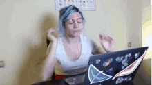 a woman with blue hair and glasses is sitting in front of a laptop computer