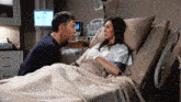 a man kisses a woman in a hospital bed with a caduceus on the monitor behind them