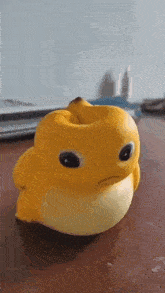 a yellow toy duck with a banana in its mouth is sitting on a wooden table .