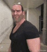 a man in a black shirt is standing in a hallway and looking at the camera .