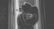 a man and a woman are hugging in front of a window in a black and white photo .