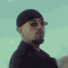 a man with a beard and sunglasses is wearing a beanie and a jacket .