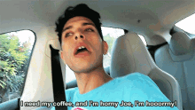 a man in a blue shirt is sitting in a car and says i need my coffee