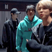 a group of young men are standing next to each other . one of the men is wearing a green hoodie .