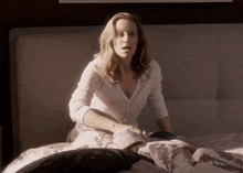 a woman is sitting on a bed with her mouth open and a surprised look on her face .