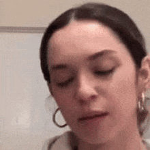 a woman wearing hoop earrings and a hoodie is making a funny face .