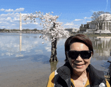 a woman wearing sunglasses and a north face vest smiles in front of a lake
