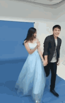a man and a woman are holding hands and dancing in a room . the woman is wearing a light blue dress .