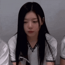 a girl with long black hair is wearing a white shirt and looking at the camera .