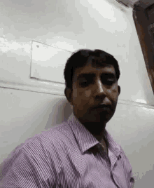 a man in a striped shirt is standing in front of a white wall and taking a selfie .