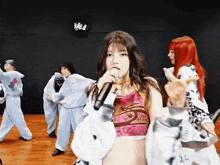 a girl singing into a microphone in front of a group of people in costume