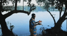 a man in a blue shirt is standing near a lake