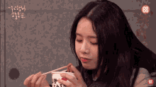 a woman is eating noodles with chopsticks from a cup that says ' r & r ' on it