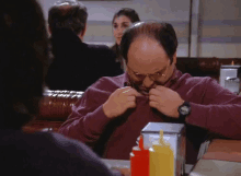 a man wearing glasses sits at a table with condiments in front of him