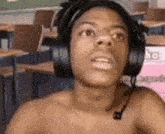 a shirtless young man wearing headphones and a microphone is sitting in a classroom .