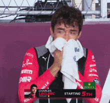 a man wipes his face with a towel while wearing a red and black jacket that says rolex