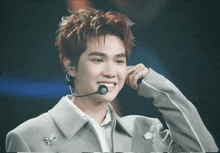 a young man wearing a microphone and smiling with his hand on his face