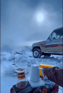 a cup of coffee sits on a table in front of a snowy car