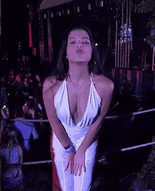a woman in a white dress is blowing a kiss in front of a crowd of people at a concert .