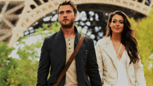 a man and a woman walking in front of the eiffel tower