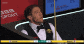 a man in a tuxedo is playing snooker in front of a screen that says bbc sport
