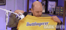 a man is holding up a yellow shirt that says buttfingerer dark web