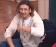 a man in a white sweater is sitting on a blue couch and smiling .