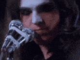 a woman with white paint on her face is singing into a pair of microphones