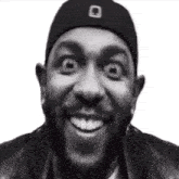 a black and white photo of a man wearing a hat and a jacket making a funny face .