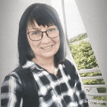a woman wearing glasses and a plaid shirt is smiling in front of a window