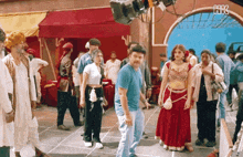 a man in a blue shirt stands in the middle of a crowd of people with hk3 on the bottom