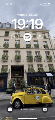 a yellow car is parked in front of a building with the time 19:19