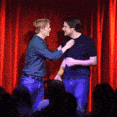 two men are standing on a stage in front of a red curtain
