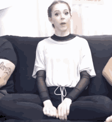 a woman sits on a black couch with a tattoo on her arm that says ' a '