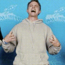 a man in a hoodie is standing in front of a blue wall and laughing .