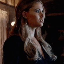 a woman with long blonde hair and earrings is standing in a dark room .