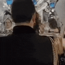 a man in a black suit is standing in front of a mirror looking at himself .