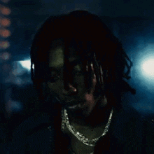 a man with dreadlocks and a chain around his neck is looking down in the dark .