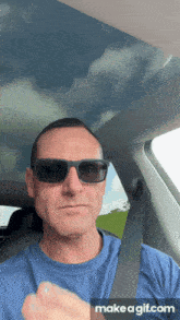 a man wearing sunglasses is sitting in a car with a make a gif.com button below him