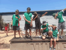a group of young boys wearing green and white shirts are standing on a bench