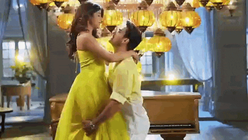 a man in a yellow shirt is holding a woman in a yellow dress in a room .