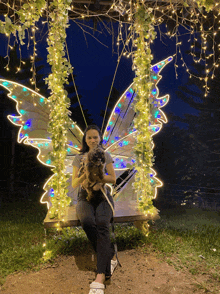 a woman is sitting on a swing with a butterfly wing decoration
