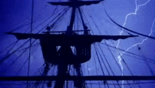 a pirate ship is silhouetted against a blue sky with lightning bolts .