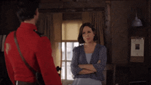 a man in a red uniform stands next to a woman in a blue dress with her arms crossed